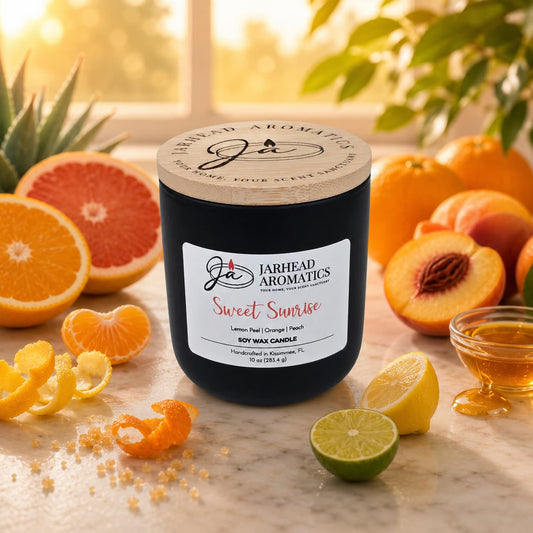 A Jarhead Aromatics Sweet Sunrise Soy Wax Candle | Bright Citrus, Agave & Peach rests on a marble surface, surrounded by sliced citrus fruits, peaches, agave, and honey as sunlight filters through lush greenery. The uplifting aroma of this candle fills the air with the fresh promise of morning.