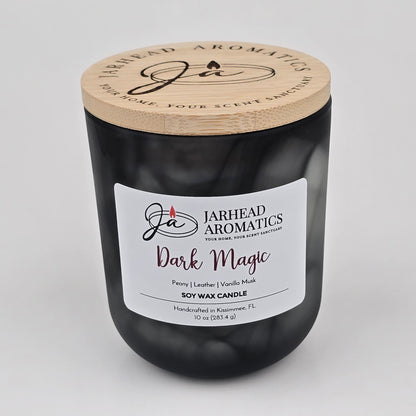A black jar candle with a wooden lid labeled Jarhead Aromatics, featuring the scent Dark Magic—a blend of peach plum, violet, leather, and patchouli. This Dark Magic Soy Wax Candle is handcrafted in Kissimmee, FL and offers a captivating Halloween-inspired aroma for those seeking an enchanting ambiance.