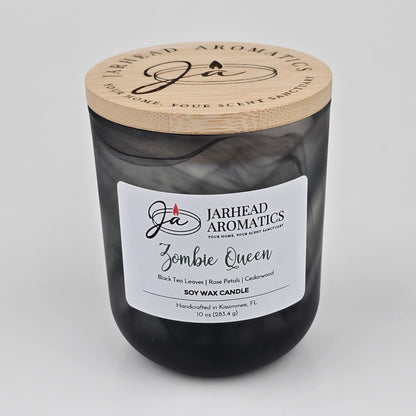 The Jarhead Aromatics Zombie Queen Soy Wax Candle is housed in a black glass jar with a wooden lid and features an enchanting blend of black tea, rose petals, and cedarwood. Handcrafted in Kissimmee, FL, this gothic Halloween candle offers the perfect fragrance for any occasion.