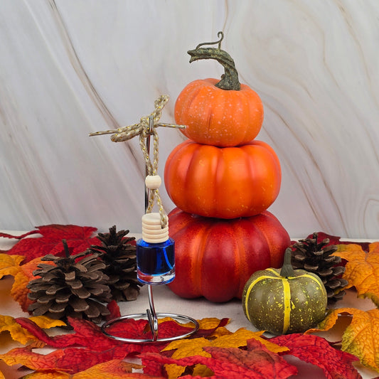 The Cozy Solace Car Diffuser from Jarhead Aromatics Fall Collection features autumn leaves, pinecones, stacked pumpkins, a green pumpkin, and a blue glass ornament with a wooden bead, capturing oak moss freshness over marble accents.