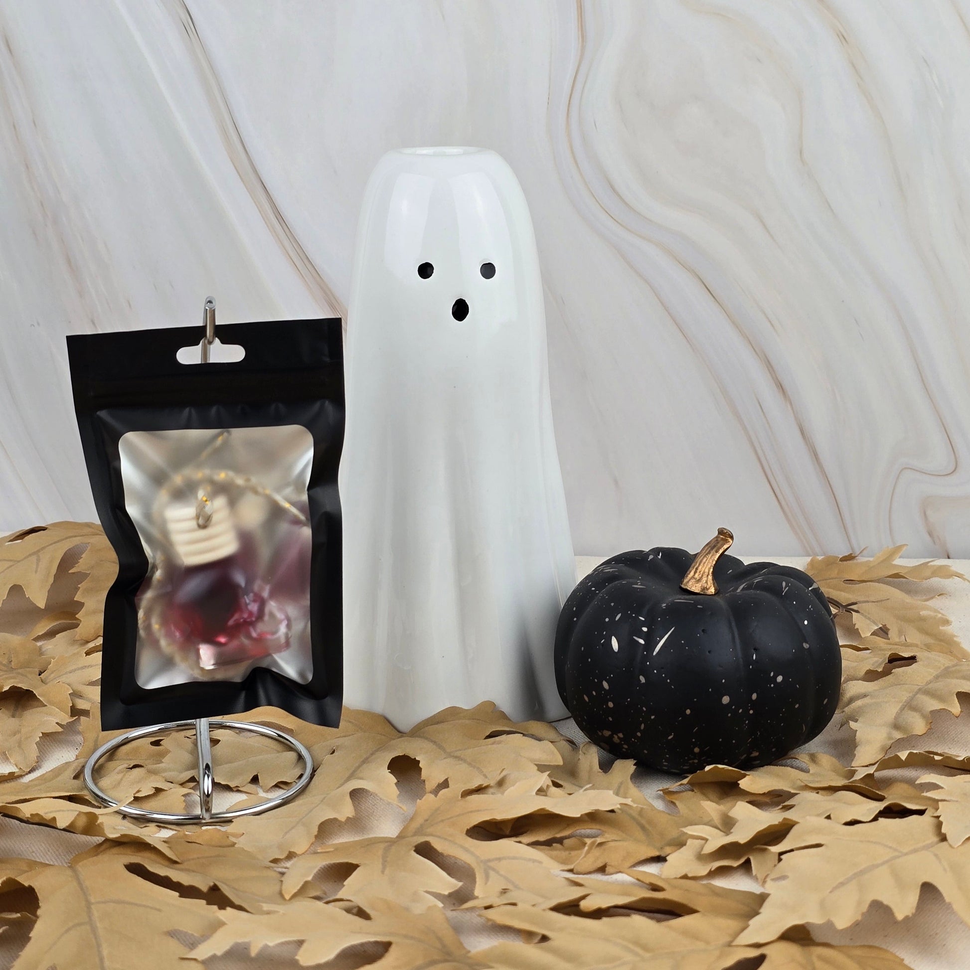 The Dark Magic Car Diffuser from Jarhead Aromatics Halloween Collection sits on dried leaves with ghost and pumpkin décor, adding a hint of mystery against a marble-patterned background.