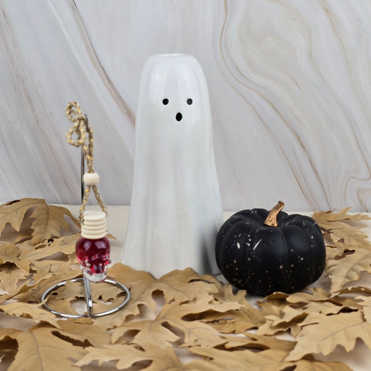 The Dark Magic Car Diffuser from Jarhead Aromatics’ Halloween Collection sits with a white ceramic ghost and black pumpkin on dried leaves, set against a marble-patterned background.