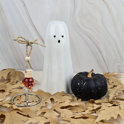 The Six Feet Under Car Diffuser from Jarhead Aromatics Halloween Collection rests on dried leaves with earthy moss, creating a festive seasonal display against a light marbled background.