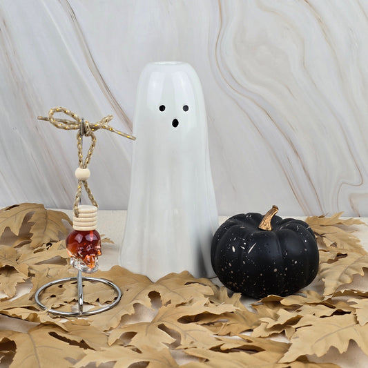 The Six Feet Under Car Diffuser from Jarhead Aromatics Halloween Collection rests on dried leaves with earthy moss, creating a festive seasonal display against a light marbled background.