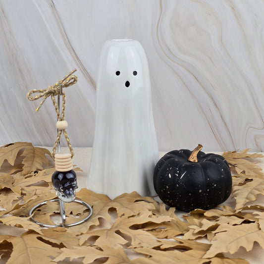 The Witches Cauldron Car Diffuser by Jarhead Aromatics from the Halloween Collection rests on dried brown leaves against a marbled backdrop, filling the air with patchouli and essential oils for an enchanting seasonal vibe.