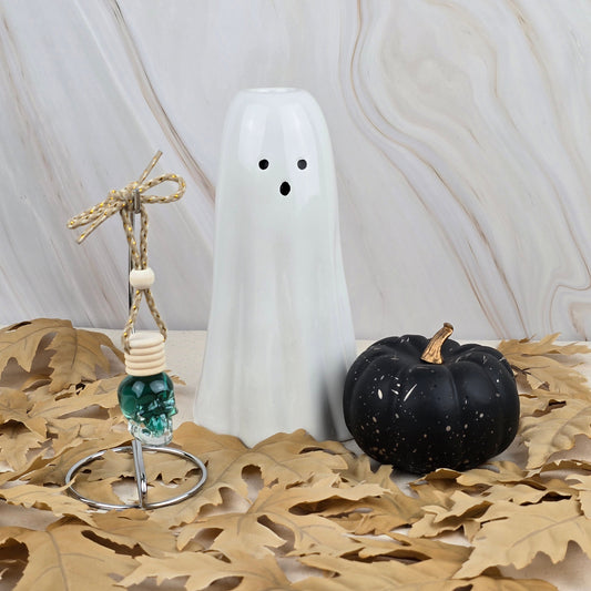 The Jarhead Aromatics Zombie Queen Car Diffuser from the Halloween Collection sits among fall leaves with a white ceramic ghost and black pumpkin, all set against a marbled backdrop for a haunting effect.