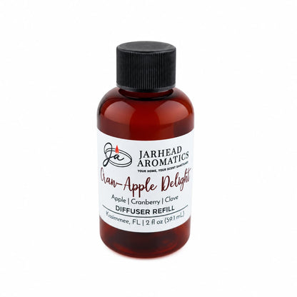A brown bottle labeled Jarhead Aromatics Cran-Apple Delight Diffuser Refill features notes of cranberry, apple, and warm cinnamon. The 2 fl oz (59.1 mL) bottle is topped with a black cap and offers an inviting autumn fragrance—perfect for creating a cozy atmosphere at home.