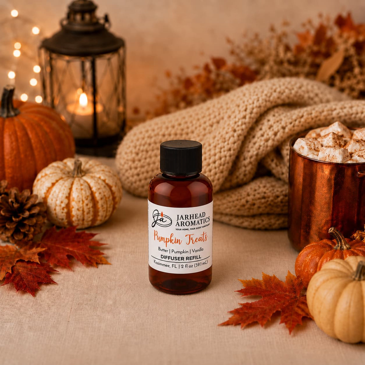 A bottle of Jarhead Aromatics Pumpkin Treats Diffuser Refill, featuring notes of pumpkin, caramel, and maple pecan, sits on a table with autumn leaves, pumpkins, a lantern, pinecones, a cozy knit blanket, and a mug of hot cocoa topped with marshmallows in a warm fall setting—creating the perfect autumn home fragrance experience.