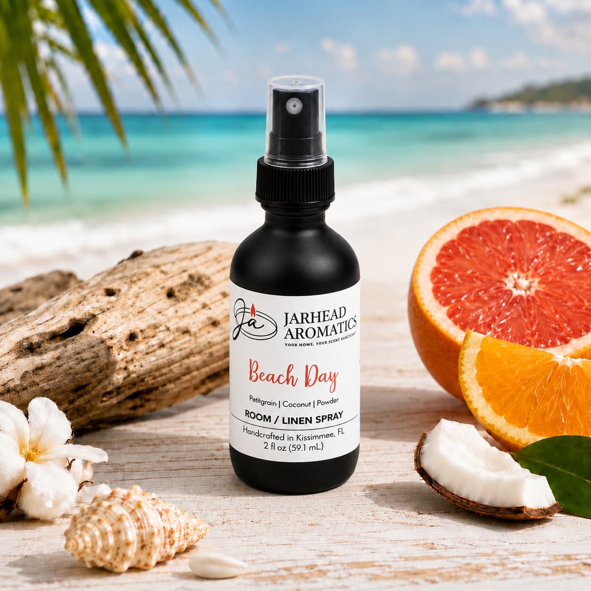 A spray bottle of Jarhead Aromatics Beach Day Room & Linen Spray | Citrus, Coconut & Coastal Musk rests on sand surrounded by orange and coconut slices, seashells, and set against a backdrop of blue ocean waters and palm trees—evoking the refreshing essence of this tropical home fragrance.