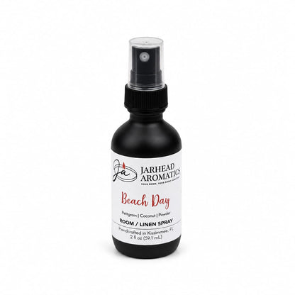 A sleek black spray bottle labeled Jarhead Aromatics Beach Day Room & Linen Spray | Citrus, Coconut & Coastal Musk features a blend of citrus, coconut, and coastal musk notes. Handcrafted in Kissimmee, FL, this 2 fl oz tropical room and linen spray infuses your home with the fresh essence of a beach-inspired fragrance for both linens and living spaces.