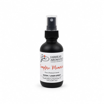 A black spray bottle labeled Jarhead Aromatics Campfire Memories Room & Linen Spray—with notes of maple, clove, and smoky embers (2 fl oz)—displayed on a white background; a unique home fragrance and campfire-inspired room spray perfect for adding warmth to any space.