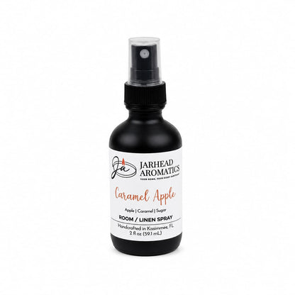 A black spray bottle labeled Jarhead Aromatics Caramel Apple Room & Linen Spray features notes of crisp apple, caramel, and warm spice. The label highlights that the product is handcrafted in Kissimmee, FL. This Caramel Apple Room & Linen Spray is perfect for filling your home with a cozy fall fragrance or refreshing your linens with a sweet autumn scent.