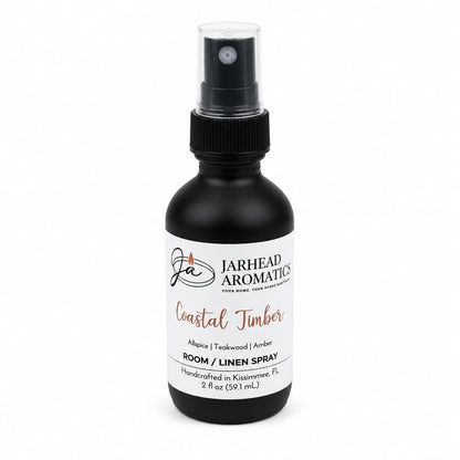 A black 2 fl oz spray bottle from Jarhead Aromatics, this Coastal Timber Room & Linen Spray features a white label with black and orange text. Enjoy a luxurious woodsy home fragrance with notes of teakwood, leather, and warm amber.