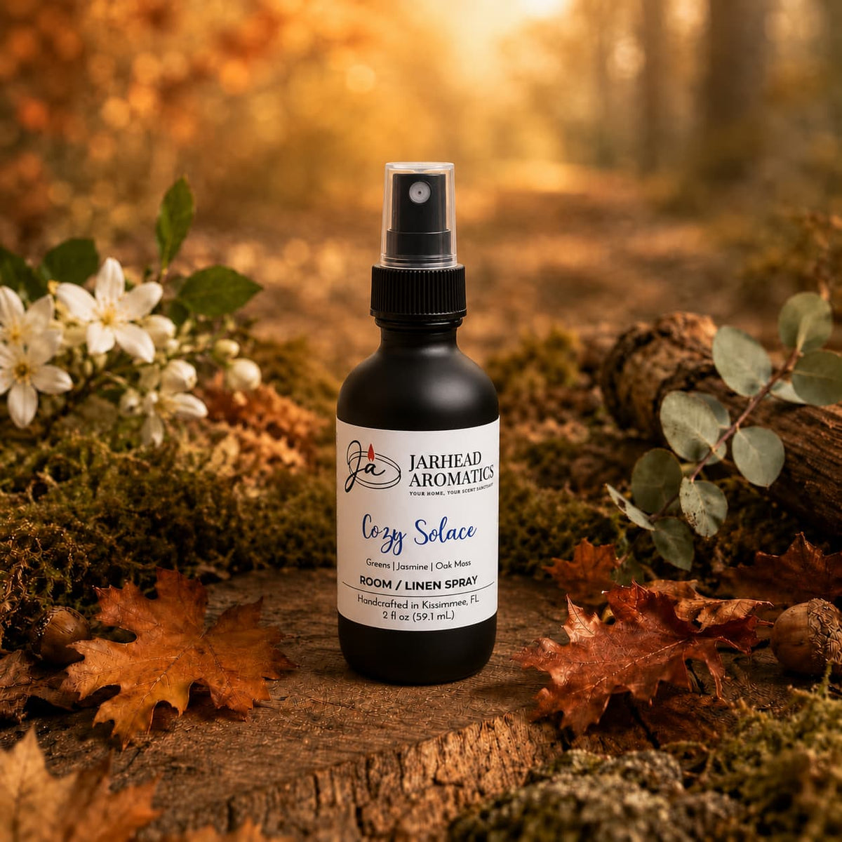 A bottle of Jarhead Aromatics Cozy Solace Room & Linen Spray | Fresh Greens, Jasmine & Oak Moss rests on a forest floor strewn with autumn leaves, flowers, and logs, bathed in warm, blurred sunlight—a perfect home fragrance that blends fresh greens with delicate jasmine and subtle oak moss notes.