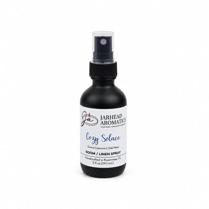 A black spray bottle labeled “Jarhead Aromatics Cozy Solace Room & Linen Spray” is displayed on a white background. This luxurious 2 fl oz (59.1 ml) room and linen spray features fresh greens, jasmine, and oak moss scents and is handcrafted in Kissimmee, FL.