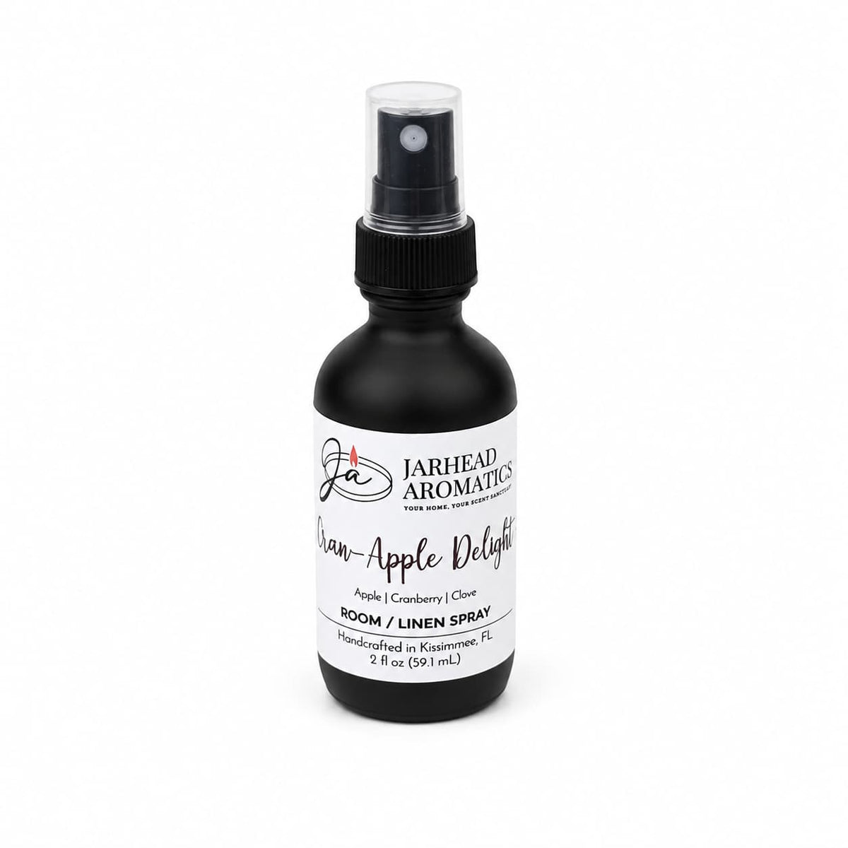 A black spray bottle labeled Jarhead Aromatics Cran-Apple Delight Room & Linen Spray is shown against a white background, featuring a cozy fruit and spice scent with notes of cranberry, apple, and warm cinnamon, designed to refresh your home.