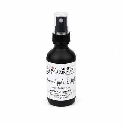 A black spray bottle labeled Jarhead Aromatics Cran-Apple Delight Room & Linen Spray is shown against a white background, featuring a cozy fruit and spice scent with notes of cranberry, apple, and warm cinnamon, designed to refresh your home.