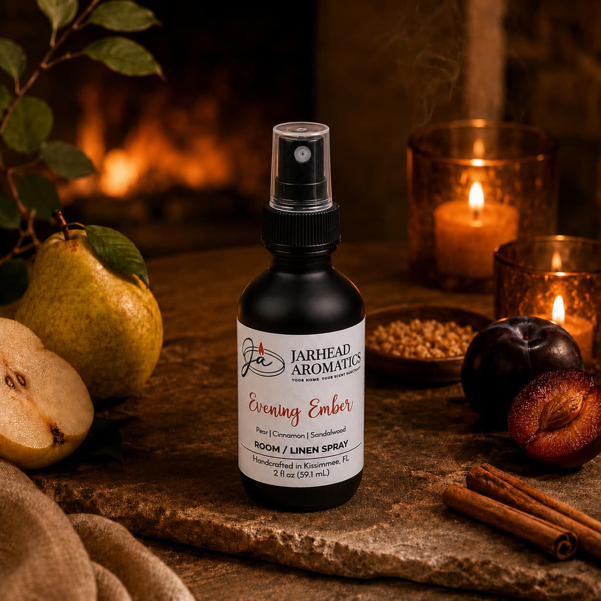 A bottle of Jarhead Aromatics Evening Ember Room & Linen Spray | Plum, Sandalwood & Soft Smoke rests on a table adorned with pears, plums, cinnamon sticks, a glowing candle, and autumn-inspired decor—filling the space with a cozy and warm atmosphere enriched by sandalwood notes and an inviting home fragrance.