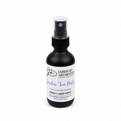 A black spray bottle labeled Jarhead Aromatics Garden Tea Party Room & Linen Spray, 2 fl oz, features a garden-inspired fragrance with notes of Rose, Lilac, and Jasmine for a delightful floral home scent experience.