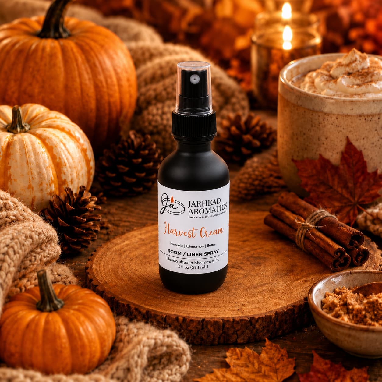 A bottle of Jarhead Aromatics Harvest Cream Room & Linen Spray | Pumpkin Spice, Brown Sugar & Vanilla Cream rests on a wooden surface amidst mini pumpkins, pinecones, cinnamon sticks, and a creamy beverage. Warm lighting and scattered fall leaves complete the scene, evoking a cozy autumn ambiance with this true gourmand home fragrance that captures the seasonal essence.