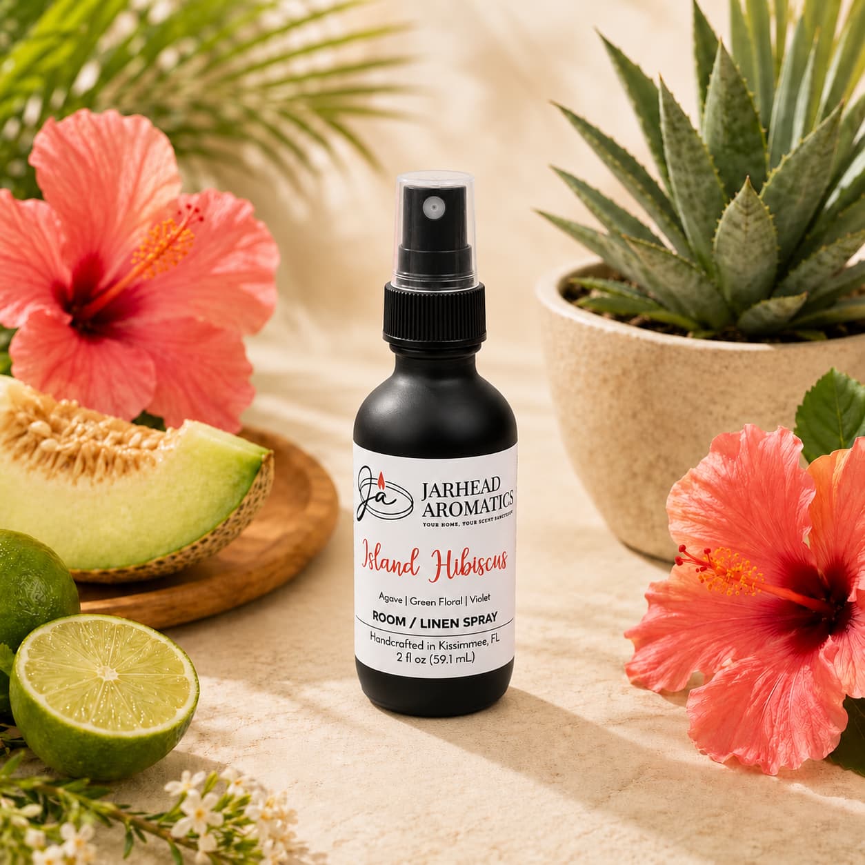 A bottle of Jarhead Aromatics Island Hibiscus Room & Linen Spray | Honeydew, Lime & Tropical Florals is surrounded by hibiscus flowers, sliced honeydew melon, a halved lime, and a potted succulent on a beige surface. This tropical spray instantly revitalizes your space with the vibrant essence of island blooms paired with fresh honeydew and zesty lime.
