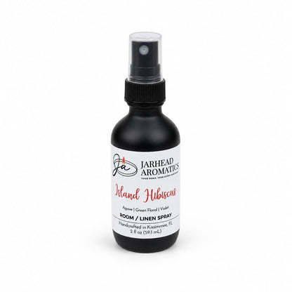 A black spray bottle labeled Jarhead Aromatics Island Hibiscus Room & Linen Spray in the Honeydew, Lime & Tropical Florals scent, featuring a refreshing tropical fragrance. This spray holds 2 fl oz and is handcrafted in Kissimmee, FL.