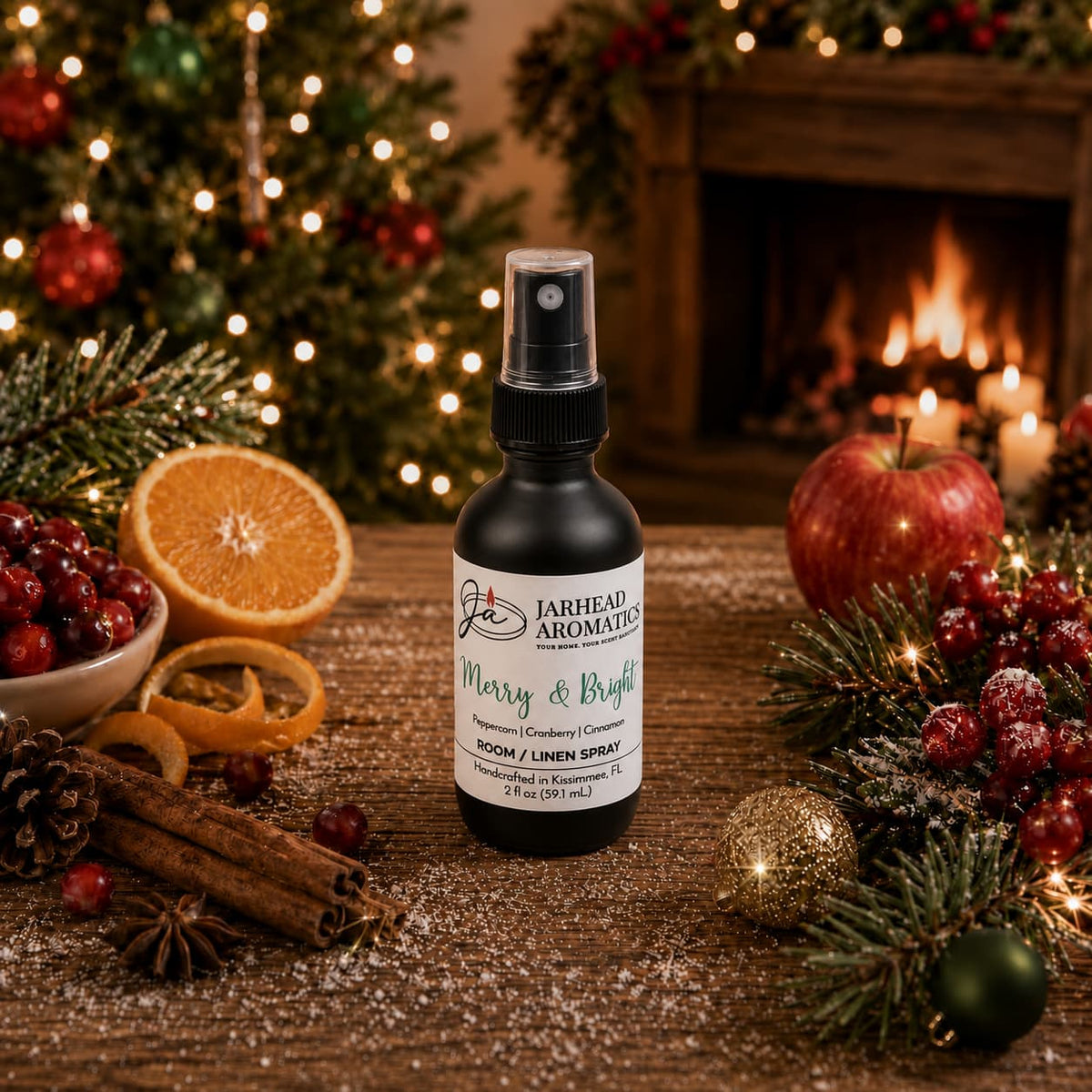 A Merry & Bright Room & Linen Spray by Jarhead Aromatics sits on a wooden table surrounded by holiday spices, cranberries, orange slices, cinnamon sticks, and evergreen branches in front of a fireplace and Christmas tree.