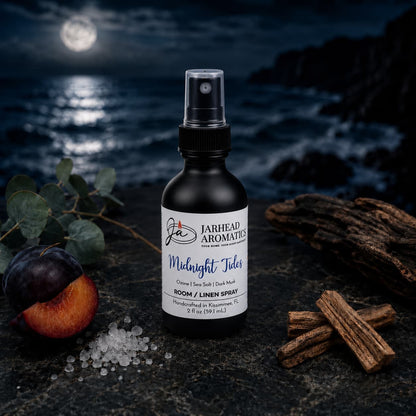 A bottle of Jarhead Aromatics’ Midnight Tides Room & Linen Spray—blending sea salt, sandalwood, and dark musk—rests atop a dark rock, its coastal scent capturing the freshness of a moonlit ocean beneath a cloudy night sky.