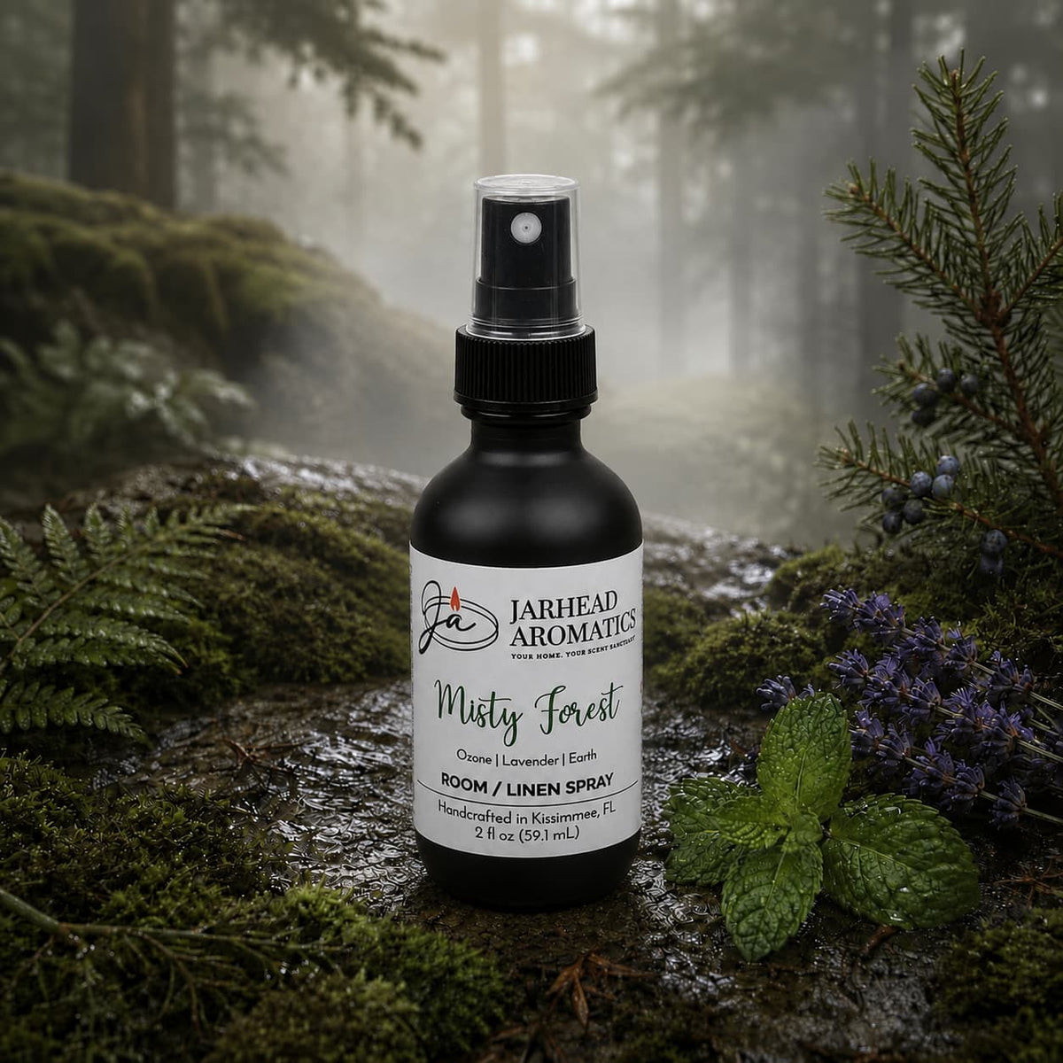 A bottle of Misty Forest Room & Linen Spray | Ozone, Moss & Juniper by Jarhead Aromatics rests on a moss-draped log in a mist-shrouded forest, encircled by lush ferns, vibrant purple blooms, and fresh greenery—a fitting scene for this nature-inspired home fragrance that captures the enchanting aroma of ozone, moss, and juniper.