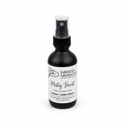 A black spray bottle labeled Jarhead Aromatics Misty Forest Room & Linen Spray | Ozone, Moss & Juniper offers a refreshing woodland scent with notes of ozone, moss, and juniper. This nature-inspired home fragrance is handcrafted in Kissimmee, FL, and comes in a 2 fl oz (59 ml) capacity.