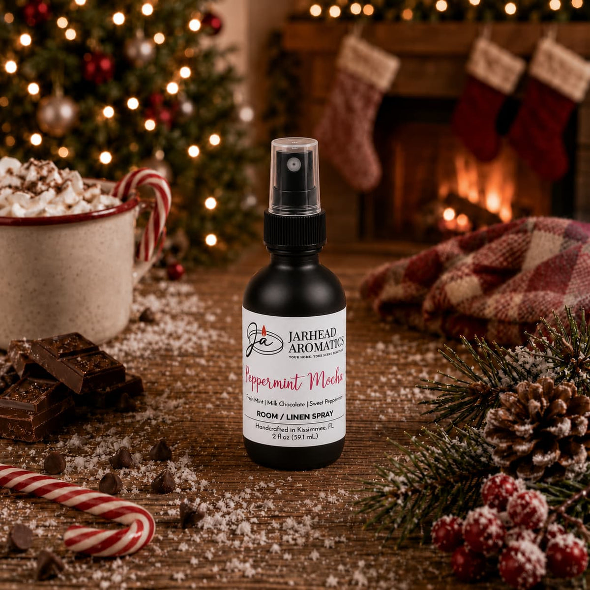 A bottle of Jarhead Aromatics Peppermint Mocha Room & Linen Spray sits on a wooden table surrounded by a mug of hot cocoa, chocolate pieces, a candy cane, and a pine branch.