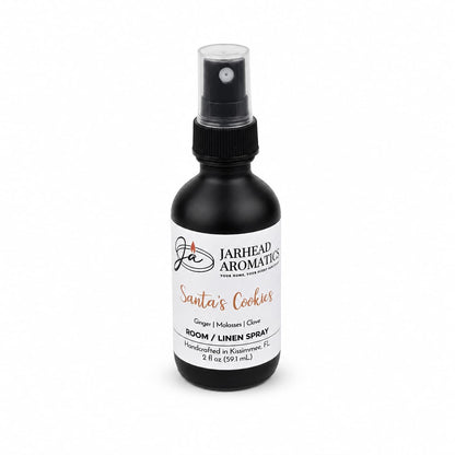 A small black spray bottle of Santa’s Cookies Room & Linen Spray, featuring a white label with notes of ginger, molasses, and clove.