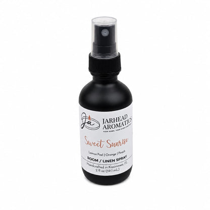 A black spray bottle of Jarhead Aromatics Sweet Sunrise Room & Linen Spray, featuring lemon, orange, peach, and citrus scents, offers a refreshing fruity fragrance for your home. This 2 fl oz spray comes with a clear cap for convenient use.