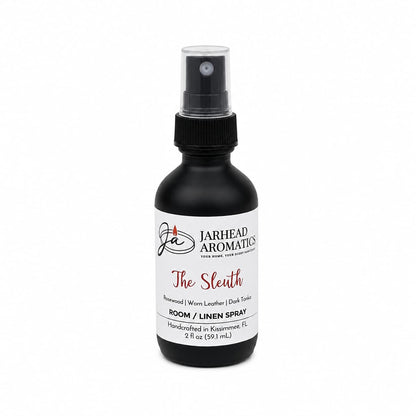 A black spray bottle labeled “The Sleuth Room & Linen Spray | Leather, Rosewood & Sandalwood” by Jarhead Aromatics features notes of rosewood, worn leather, sandalwood, and dark tonic. This handcrafted 2 fl oz home fragrance is made in Kissimmee, FL—perfect for refreshing any room or linens.