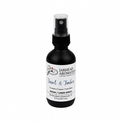 A small black spray bottle with a white label reading Tinsel & Timber Room & Linen Spray | Eucalyptus, Pine, Smoke & Tonka, a winter forest scent.