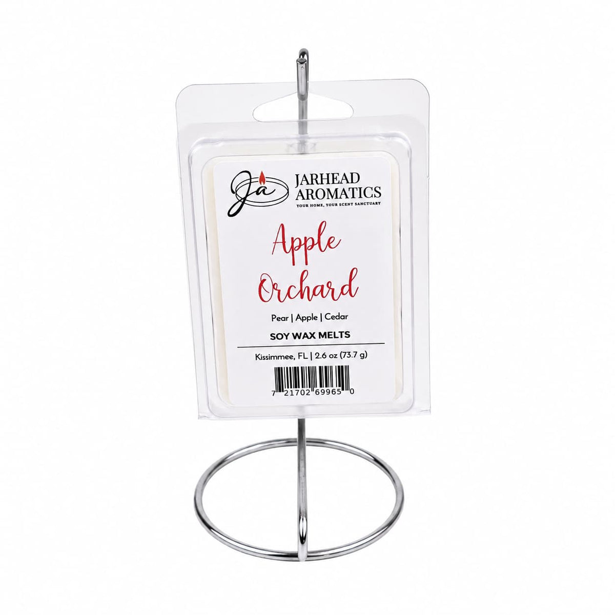 A 2.6 oz package of Jarhead Aromatics Apple Orchard Soy Wax Melt | Crisp Apple, Juicy Pear & Cedarwood rests on a metal holder. The label highlights notes of crisp apple, juicy pear, and cedarwood. Enjoy hours of long-lasting fragrance as this soy wax melt fills your space with the fresh scent of an orchard in bloom.