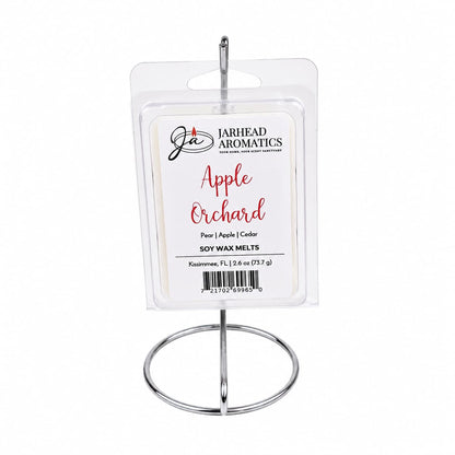 A 2.6 oz package of Jarhead Aromatics Apple Orchard Soy Wax Melt | Crisp Apple, Juicy Pear & Cedarwood rests on a metal holder. The label highlights notes of crisp apple, juicy pear, and cedarwood. Enjoy hours of long-lasting fragrance as this soy wax melt fills your space with the fresh scent of an orchard in bloom.