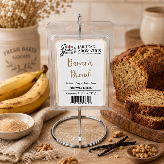 A package of Jarhead Aromatics Banana Bread Soy Wax Melt | Ripe Banana, Walnut & Warm Vanilla is displayed on a stand, surrounded by sliced banana bread, bananas, walnuts, vanilla beans, a bowl of sugar, and a container labeled Fresh Baked Goods. Infused with the comforting aroma of homemade banana nut bread—featuring notes of ripe banana, walnut, and warm vanilla—these melts fill your space with a welcoming and long-lasting fragrance.