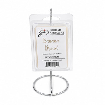 A package of Jarhead Aromatics Banana Bread Soy Wax Melt | Ripe Banana, Walnut & Warm Vanilla is displayed upright on a silver metal stand against a white background, showcasing its homemade-inspired fragrance with notes of ripe banana, walnut, and warm vanilla.