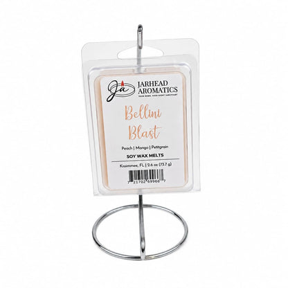 A package of Jarhead Aromatics Bellini Blast Soy Wax Melt | Tangerine, Peach & Tropical Mango sits on a silver metal display stand. The label highlights scent notes of tangerine, peach, and tropical mango, with a product weight of 6.2 oz (175 g), offering a vibrant tropical fragrance in every soy wax melt.