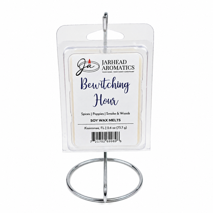 A package of Jarhead Aromatics Bewitching Hour Soy Wax Melt | Exotic Spices, Dark Florals & Smoky Woods rests on a metal stand. The label highlights alluring notes of exotic spices, dark florals, and smoky woods—promising a long-lasting fragrance that enchants your space. Each mystical wax melt has a net weight of 2.6 oz (73.7 g).