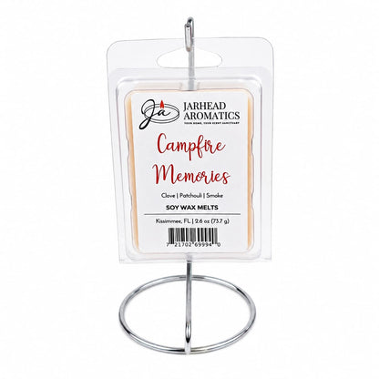 A 2.6 oz (73.7 g) package of Jarhead Aromatics Campfire Memories Soy Wax Melt sits on a silver stand, with the label highlighting notes of maple, clove, and smoky embers for an authentic campfire aroma and a long-lasting fragrance.