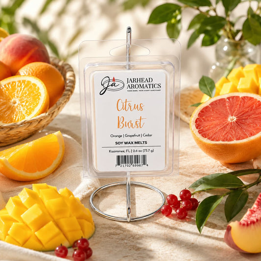 A package of Citrus Burst Soy Wax Melt by Jarhead Aromatics is displayed on a stand, surrounded by fresh oranges, grapefruit, mangoes, and berries, with a basket of fruit and green leaves in the background—a vibrant showcase of irresistible home fragrance featuring notes of orange, mango, peach, and grapefruit.