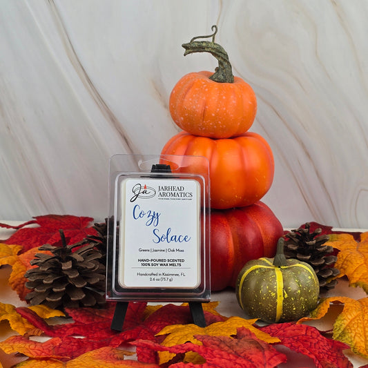 Jarhead Aromatics’ Cozy Solace - Soy Wax Melt from the Fall Collection is shown in front of pumpkins, pine cones, and autumn leaves, with notes of oak moss enhancing this warm seasonal display.