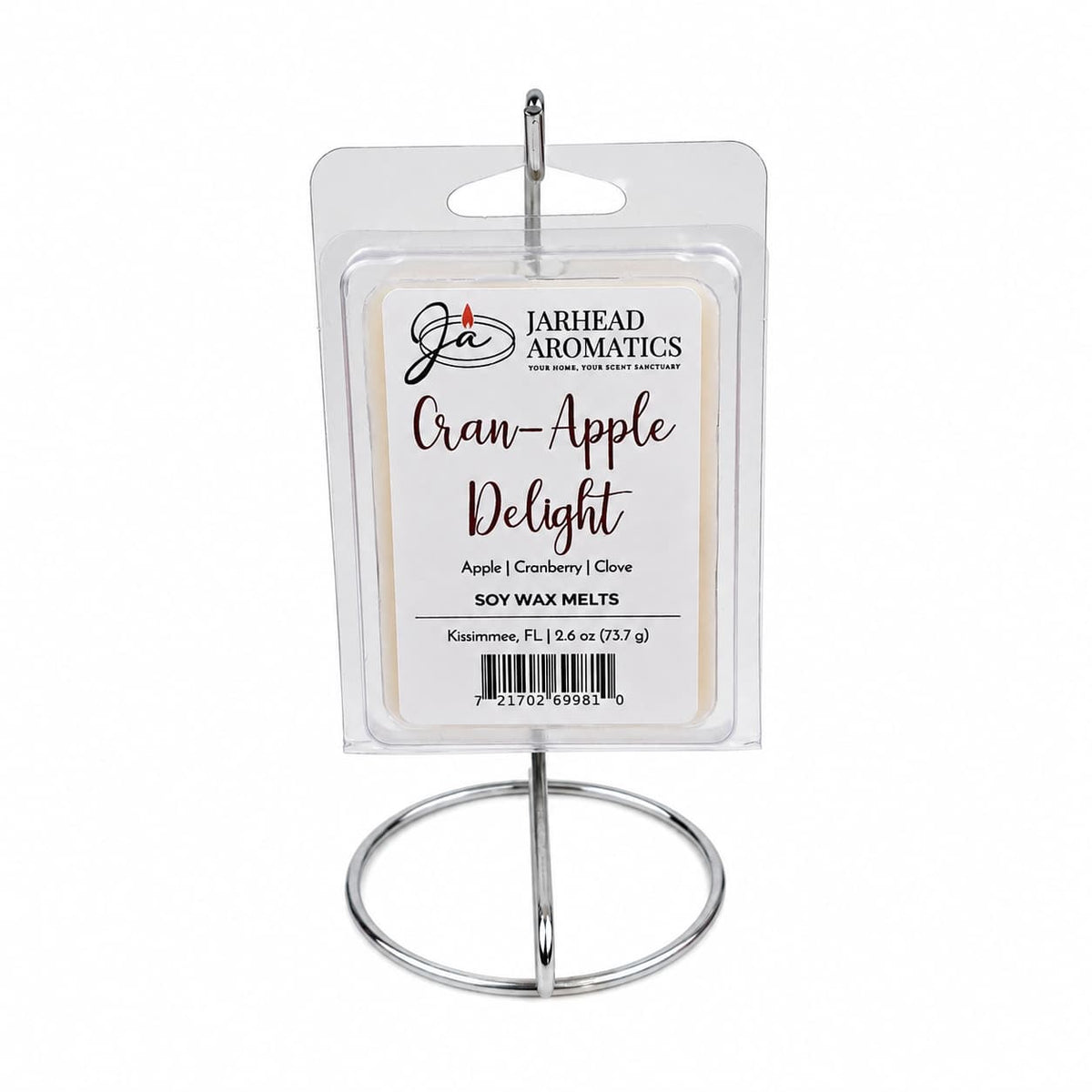A package of Jarhead Aromatics Cran-Apple Delight Soy Wax Melt is displayed elegantly on a silver stand. The label showcases this intensely fragrant soy wax melt, featuring the enticing aromas of cranberry, apple, and warm cinnamon, along with product information and a barcode.
