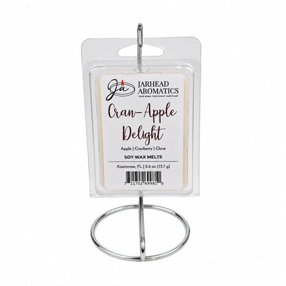 A package of Jarhead Aromatics Cran-Apple Delight Soy Wax Melt is displayed elegantly on a silver stand. The label showcases this intensely fragrant soy wax melt, featuring the enticing aromas of cranberry, apple, and warm cinnamon, along with product information and a barcode.