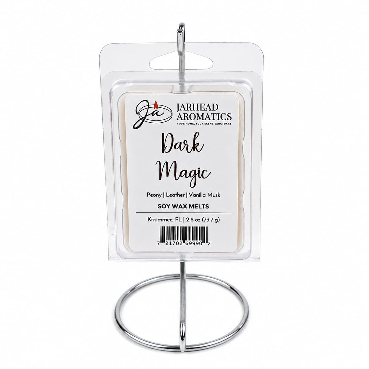 A pack of Jarhead Aromatics Dark Magic Soy Wax Melts, featuring notes of peach, plum, dark florals, and vanilla musk, is elegantly displayed in a clear package on a silver metal stand. The label highlights the enticing fragrance profile of these scented wax melts, with a total weight of 2.6 oz.