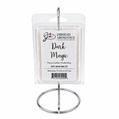 A package of Jarhead Aromatics Dark Magic Soy Wax Melt rests elegantly on a silver metal stand. The label showcases its premium fragrance notes—peach, plum, dark florals, and vanilla musk—and features a barcode, emphasizing these soy wax melts crafted with care.