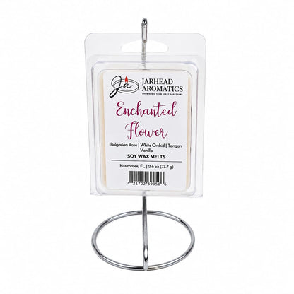A package of Jarhead Aromatics Enchanted Flower Soy Wax Melt is displayed on a silver metal stand. This fragrance blends Bulgarian rose, white orchid, vanilla, and tangerine notes.