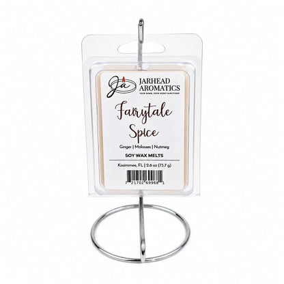 A pack of Jarhead Aromatics Fairytale Spice Soy Wax Melts—highlighting a comforting blend of gingerbread, molasses, and warm spice—is displayed on a silver metal stand. The label showcases enticing notes of ginger, molasses, and nutmeg.